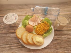 Zdjęcie przedstawia Dietę łatwostrawną:  Kawa zbożowa z mlekiem/p Bułka pszenna długa krojona  Masło extra 82% Szynkowa dębowa drobiowa kiełbasa grubo rozdrobniona Pasta warzywna  Jogurt typu islandzkiego naturalny Skyr Woda mineralna Sałata zielona Jajko gotowane